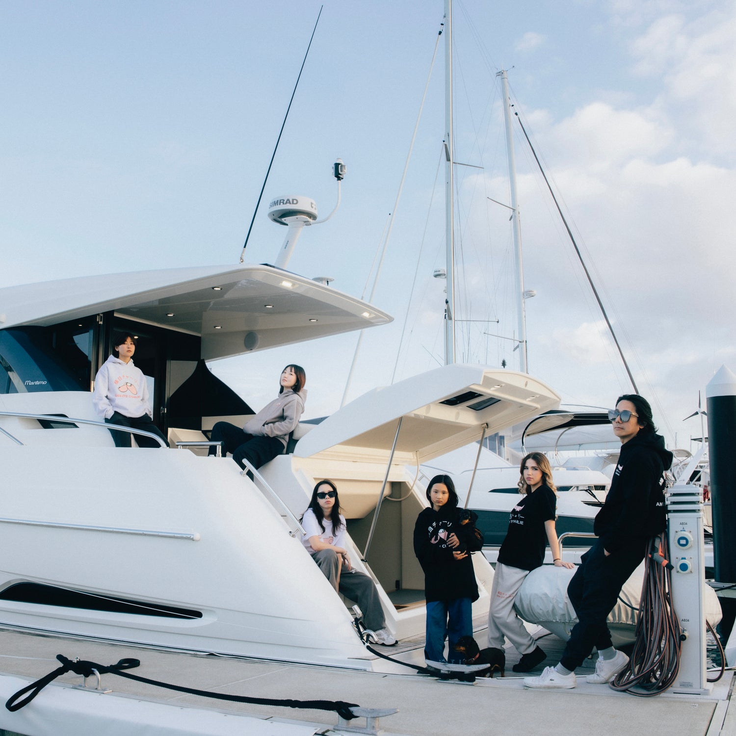 Group of people wearing hoodies and streetwear on a yacht with a clear sky background